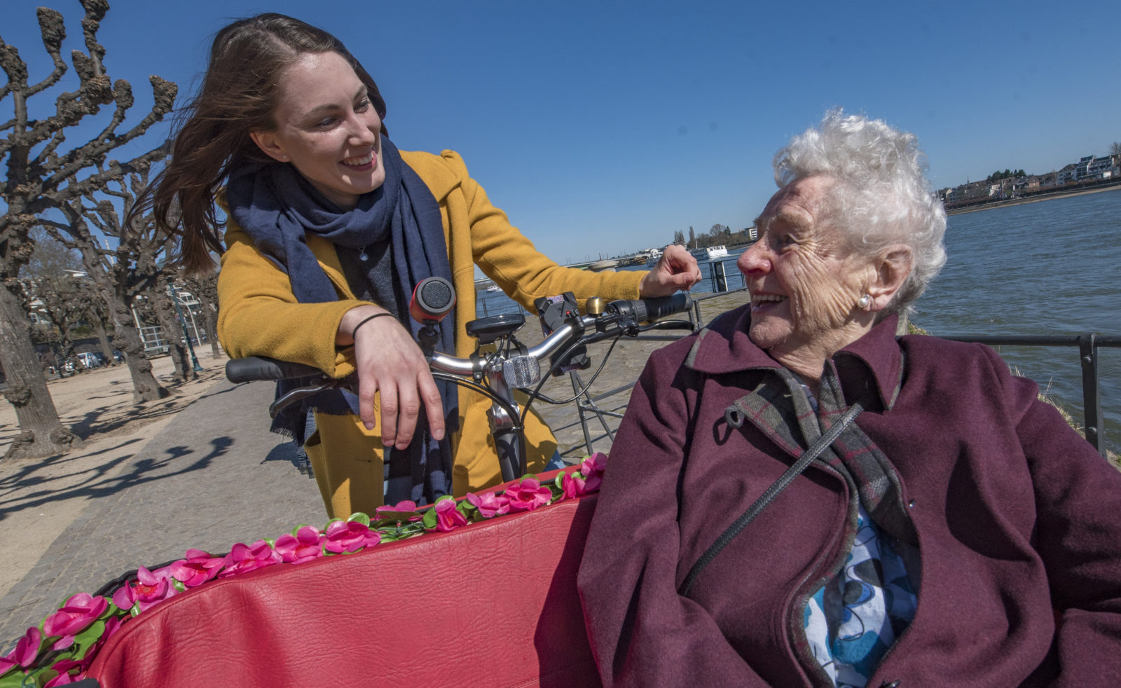 Seniorin sitzt in einer Rikscha und lächelt dir hinter ihr sitzende Pilotin an.